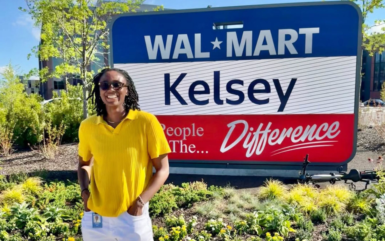 Woman standing in front of sign that reads "WALMART; Kelsey; The People, The Difference