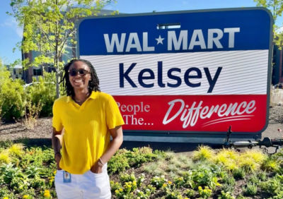 Woman standing in front of sign that reads "WALMART; Kelsey; The People, The Difference
